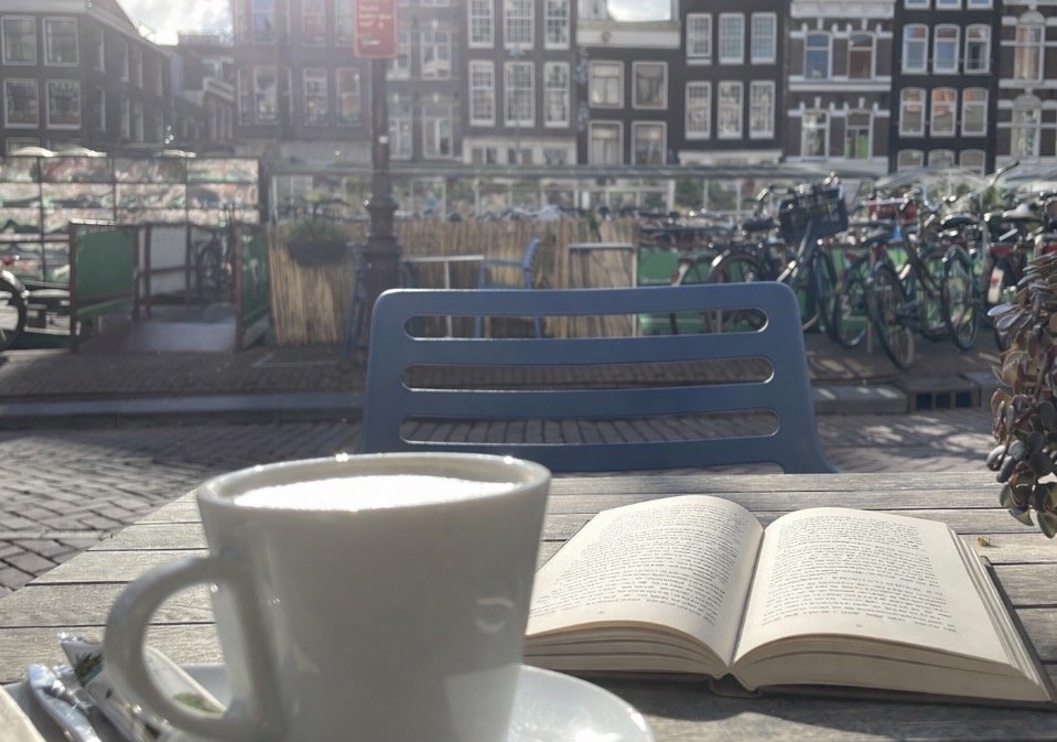 A cup of coffee and an open book on a caf&eacute; table beside a canal in Amsterdam